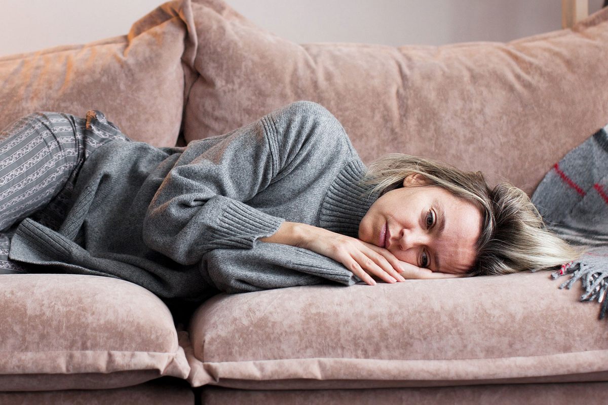 Frau liegt mit traurigem Gesichtsausdruck auf der Couch (Themenbild).