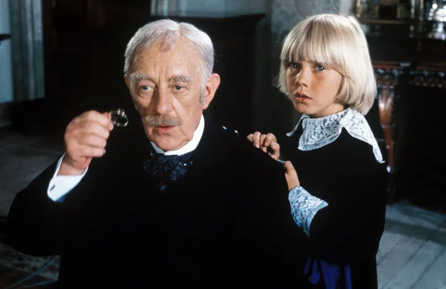 Der kleine Lord Großvater, Earl von Dorincourt, und sein Enkel der kleine Lord tragen jeweils ein schwarzes Outfit. Der Großvater schaut durch sein Einglas.
