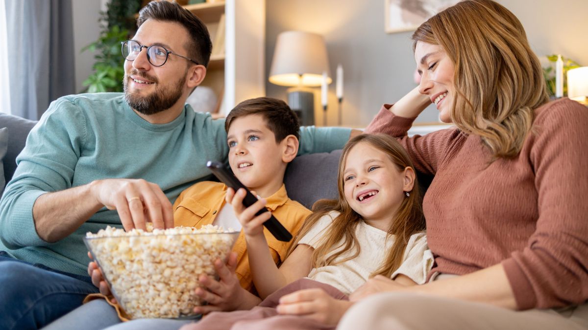 Vater, Mutter, ein Junge und ein Mädchen sitzen auf dem Sofa, gucken Fernsehen und essen Popcorn
