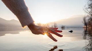 Detail der Hand berührenden Wasseroberfläche des Sees bei Sonnenuntergang. - Foto: swissmediavision / iStock