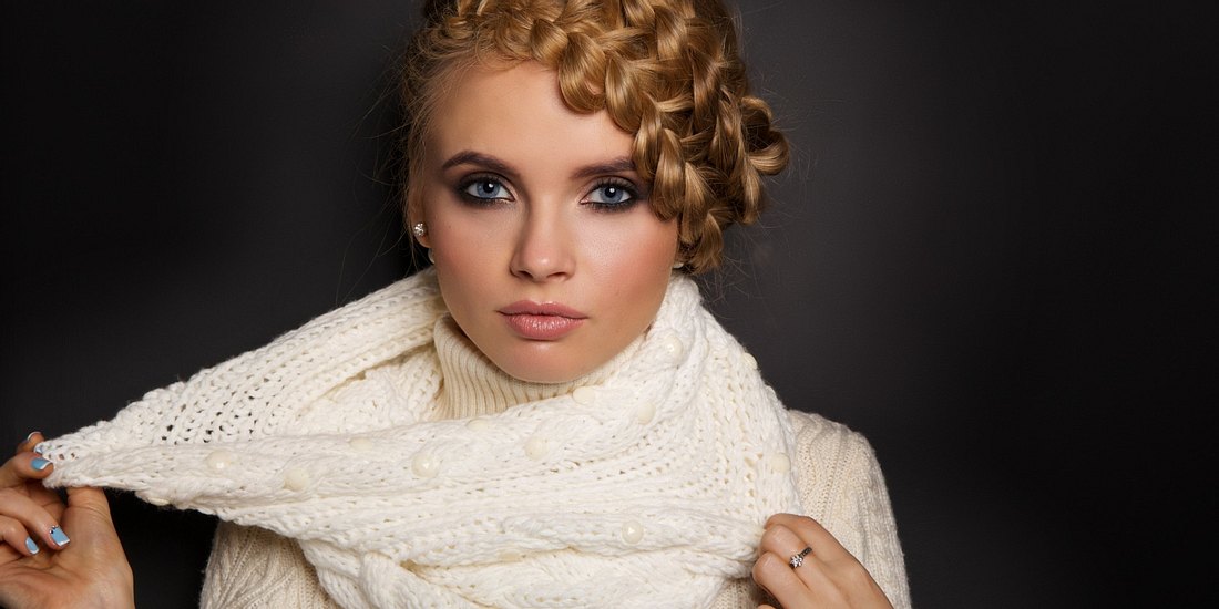 portrait of a beautiful young blonde woman on dark background. hair tied in a braid. girl wearing a warm sweater and scarf