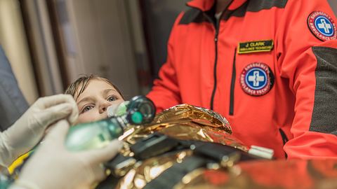 Ein Kind liegt mit Beatmungsmaske auf einer Trage. - Foto: simonkr/iStock