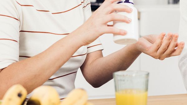 Frau, die am Tisch Vitamine verwendet. - Foto: RgStudio/iStock