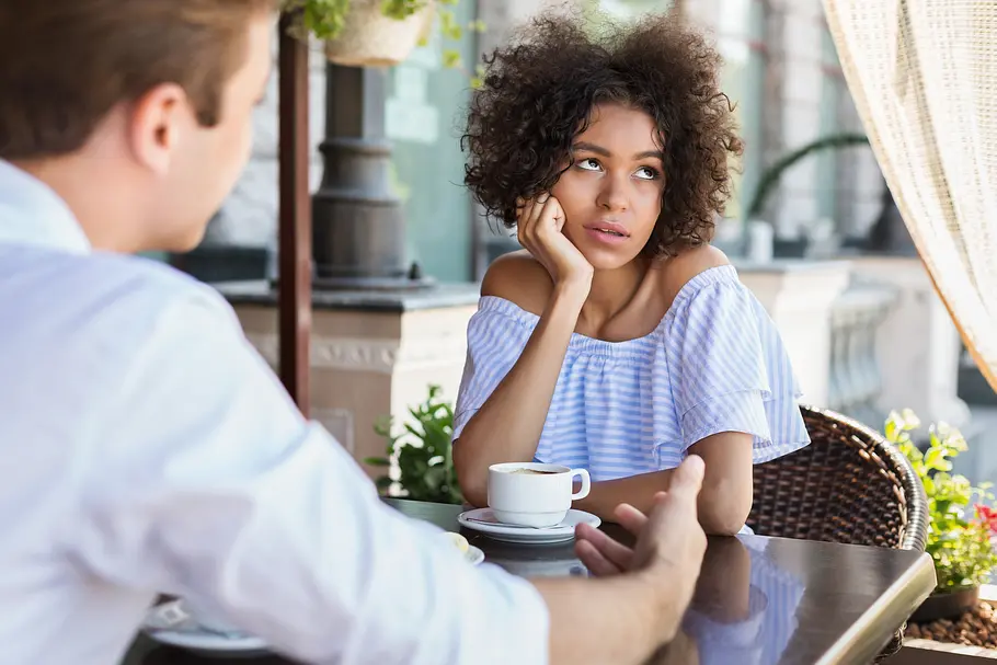 Frau sitzt an einem Tisch im Cafe und rollt mit den Augen. Links m Vordergrund der Rücken eines Mannes, der gestikuliert. Frau sitzt an einem Tisch im Cafe und rollt mit den Augen. Links m Vordergrund der Rücken eines Mannes, der gestikuliert.