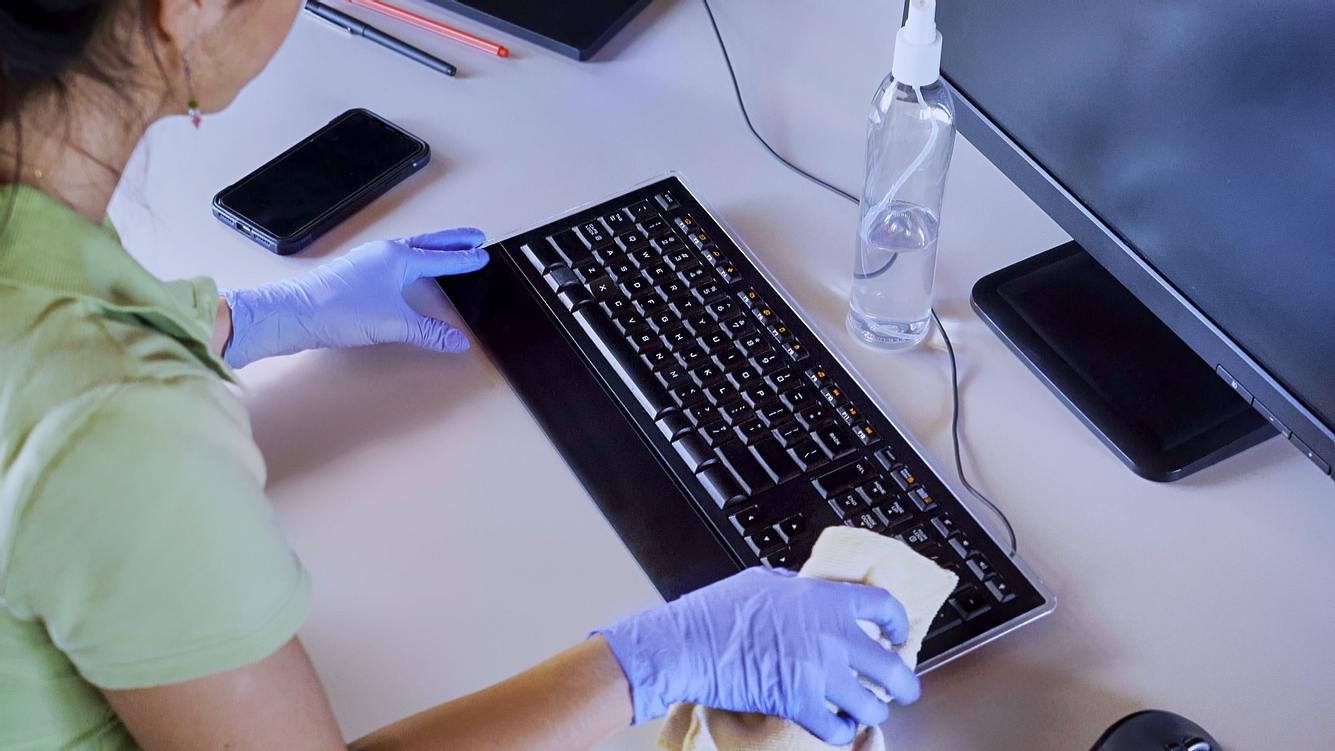 Eine Frau mit Latex-Handschuhen reinigt die Tastatur ihres Computers