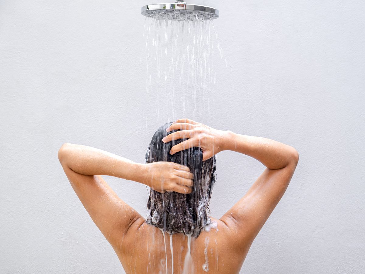 Frau wäscht ihre Haare unter der Dusche