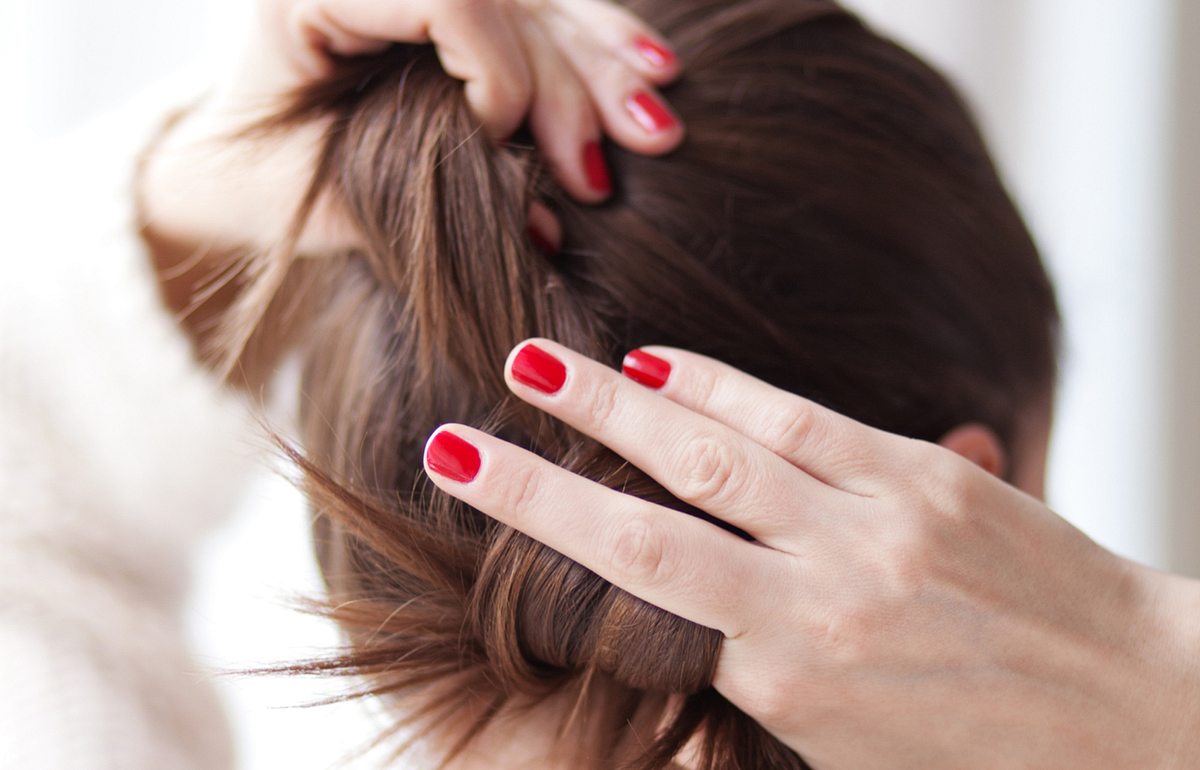 Frau mit roten Fingernägel bindet sich ihr braunes Haar.