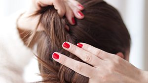 Frau mit roten Fingernägel bindet sich ihr braunes Haar. - Foto: AnaBGD/iStock (Themenbild)