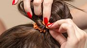 Frau macht sich mit einem Haargummi einen Dutt. - Foto: schankz/iStock (Themenbild)