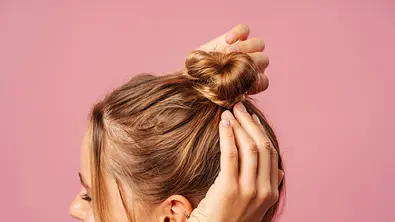 Frau bindet sich einen Dutt. - Foto: Mariia Vitkovska/iStock (Themenbild)