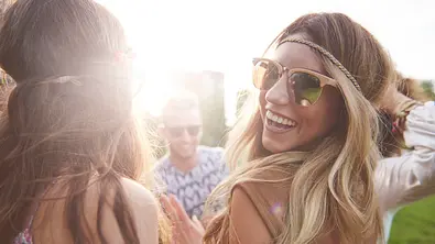 Frau mit Sonnenbrille tanzt mit Freunden und lacht in die Kamera. - Foto: gpointstudio/iStock (Themenbild)