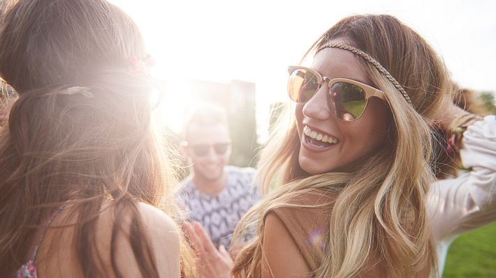 Frau mit Sonnenbrille tanzt mit Freunden und lacht in die Kamera. - Foto: gpointstudio/iStock (Themenbild)
