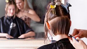 Eine Frau sitzt mit nassem und abgestecktem Haar vor einem Spiegel und bekommt von einer anderen Frau das Haar geschnitten.  - Foto: Umi Di/iStock (Themenbild)
