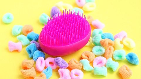 Pinke Entwirrbürste und bunte Haargummis auf gelbem Hintergrund - Foto: iStock/Satilda