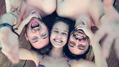 Eine junge Frau liegt lachend zwischen zwei Männern - Foto: AleksandarGeorgiev / iStock