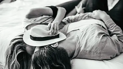 Schwarz weiß Foto eines verliebten Paares, das auf einem Bett liegt und sich küsst. Sie hält einen Hut vor ihre Gesichter. - Foto: GCShutter/iStock Schwarz weiß Foto eines verliebten Paares, das auf einem Bett liegt und sich küsst. Sie hält einen Hut vor ihre Gesichter. - Foto: GCShutter/iStock
