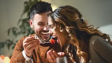 Ein verliebtes Paar am Esstisch. Er füttert sie liebevoll. - Foto: gilaxia/iStock