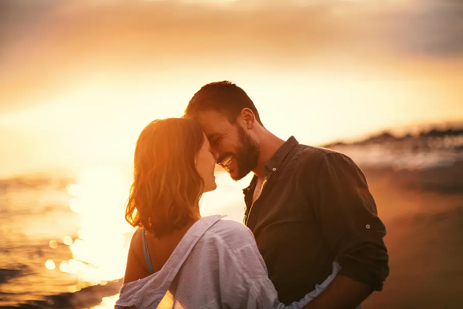 Erotische Liebesgeschichte Ein verliebtes Paar, das sich am Strand vor einem Sonnenaufgang umarmt.