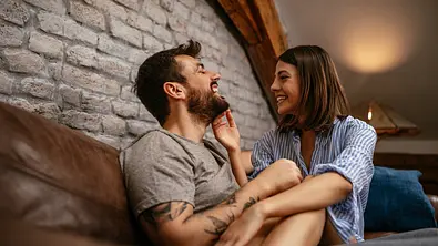 Paar teilt einen zärtlich-lustigen Moment auf dem Sofa. - Foto: bernardbodo / iStock