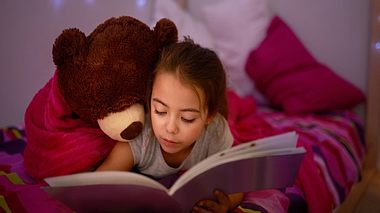 Braunhaariges Mädchen liegt lesend auf Bett - Foto: iStock/PeopleImages