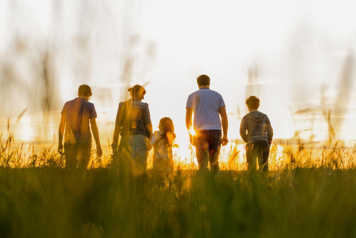 Eine Familie geht über eine Wiese der untergehenden Sonne entgegen. (Themenbild)