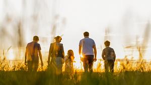 Eine Familie geht über eine Wiese der untergehenden Sonne entgegen. (Themenbild) - Foto: SimonSkafar/iStock