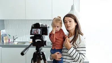 Mutter hält weinendes Kind im Arm und spricht in eine aufgestellte Kamera - Foto: iStock/blackCAT