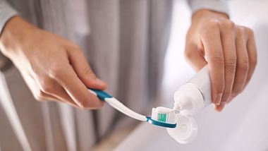 Nahaufnahme: Frauenhände, die Zahnpasta auf die Zahnbürste auftragen. - Foto: PeopleImages/iStock