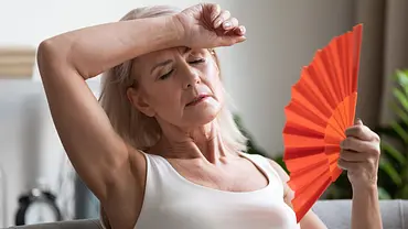Frau hat eine Hitzewelle. Sie wischt sich Schweiß von der Stirn und fächert sich Luft zu (Themenbild). - Foto: AdobeStock / fizkes Frau hat eine Hitzewelle. Sie wischt sich Schweiß von der Stirn und fächert sich Luft zu (Themenbild). - Foto: AdobeStock / fizkes