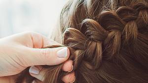 Jemand flechtet braune Haare zu einem Zopf. - Foto: Natalya Vilman/ iStock (Themenbild)