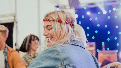 Frau mit blondem Haar und Blumenkranz tanzt auf einem Festival und lächelt.  - Foto: SolStock/iStock (Themenbild)