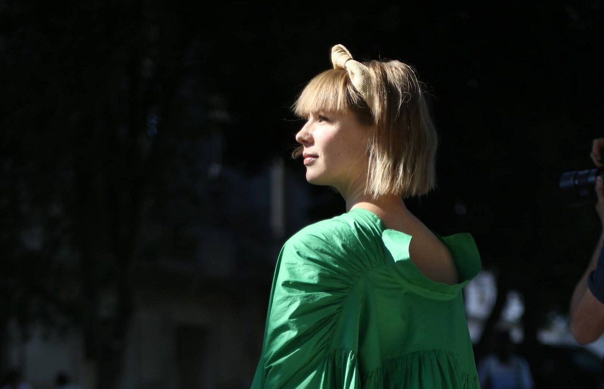 Frau mit blondem Haar und grünem Kleid schaut seitlich nach links in die Sonne.