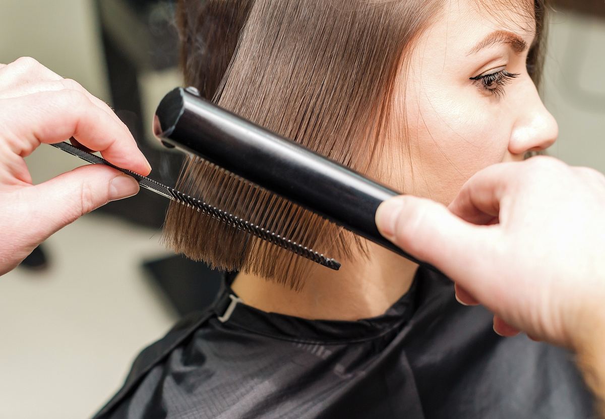 Frau mit braunen Haaren bekommt die Haare mit einem Glätteisen frisiert.