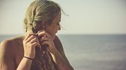 Eine Frau flechtet ihr blondes Haar. - Foto: fotostorm/iStock (Themenbild)