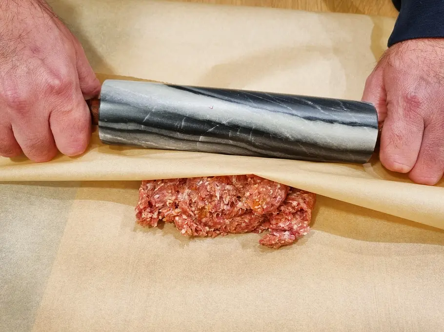 Das Hackfleisch wird zwischen zwei Lagen Backpapier ausgerollt.