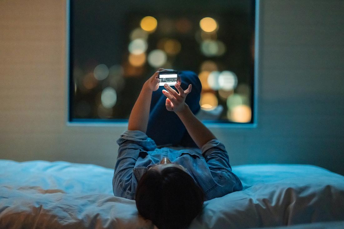 Frau liegt auf dem Bett und starrt in ihr Handy