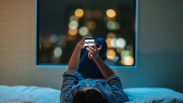 Frau liegt auf dem Bett und starrt in ihr Handy - Foto: iStock/recep-bg