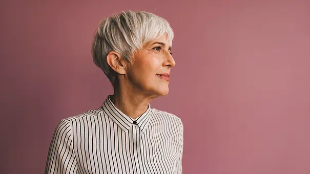 Frau mit Hemd und kurzen grauen Haaren vor rosa Wand - Foto: istock/ FreshSplash Frau mit Hemd und kurzen grauen Haaren vor rosa Wand - Foto: istock/ FreshSplash