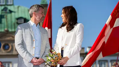 Frederik und Mary blicken sich vor Schloss Fredensborg ins Gesicht, im Hintergrund wehende Dänemarkflaggen und ein blauer Himmel. - Foto: Martin Sylvest Andersen/Getty Images