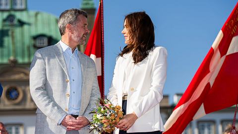 Frederik und Mary blicken sich vor Schloss Fredensborg ins Gesicht, im Hintergrund wehende Dänemarkflaggen und ein blauer Himmel. - Foto: Martin Sylvest Andersen/Getty Images