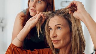 Frau sitz beim Friseur, hält ihre Haare hoch und schaut unglücklich in den Spiegel. - Foto: PeopleImages / iStock