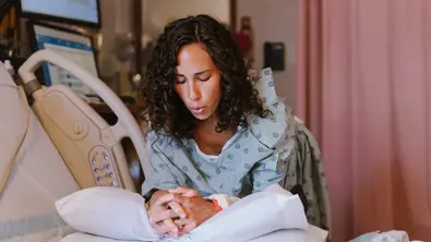 Eine Schwangere in Kittel lehnt über einem Krankenhausbett und veratmet die Wehen - Foto: iStock/Fly View Productions