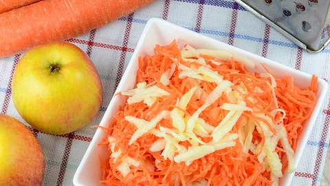 Geriebener Apfel und Karotten in einer Schale mit Äpfel, Karotten und einer Reibe daneben. - Foto: WDnet / iStock