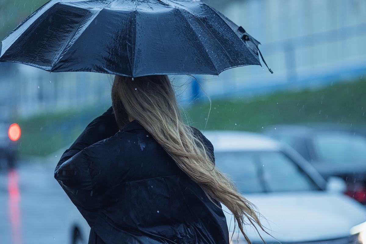 Frau hält sich im Sturm während eines Gewitters die Hand vor den Mund und dreht sich weg.