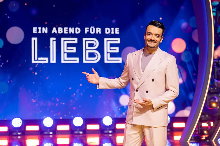 Die Giovanni Zarrella Show Die Giovanni Zarrella Show - Ein Abend für die Liebe: Giovanni Zarrella steht auf der Bühne und lächelt in die Kamera. Er deutet mit der Hand auf die Aufschrift mit dem Sendungsmotto Ein Abend für die Liebe, die im Hintergrund auf der LED-Wand zu sehen ist.