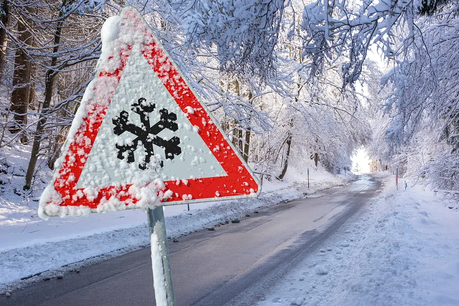 Eine glatte Straße, Schnee und ein Straßenschild mit Schneeflocken-Symbol Eine glatte Straße, Schnee und ein Straßenschild mit Schneeflocken-Symbol