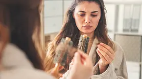 Frau steht mit Bürste vorm Spiegel und verliert viele Haare beim Kämmen - Foto: istock/ (seb_ra Frau steht mit Bürste vorm Spiegel und verliert viele Haare beim Kämmen - Foto: istock/ (seb_ra