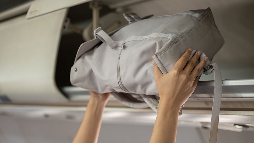Handgepäck Rucksack wird im Flugzeug von einer Frau ins Gepäckfach gegeben  - Foto: iStock / BongkarnThanyakij 