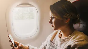 Frau sitzt im Flugzeug und hält Handy in der Hand - Foto: iStock / Oleh_Slobodeniuk Frau sitzt im Flugzeug und hält Handy in der Hand - Foto: iStock / Oleh_Slobodeniuk