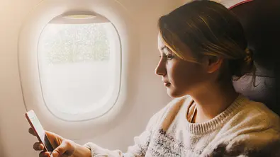 Frau sitzt im Flugzeug und hält Handy in der Hand - Foto: iStock / Oleh_Slobodeniuk